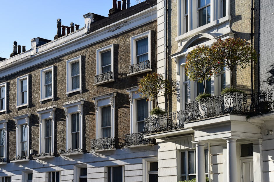 A row of elegant white terraced buildings with classic architectural features, including ornate window frames and decorative cornices, situated along a street. The ground floors have small gardens enc