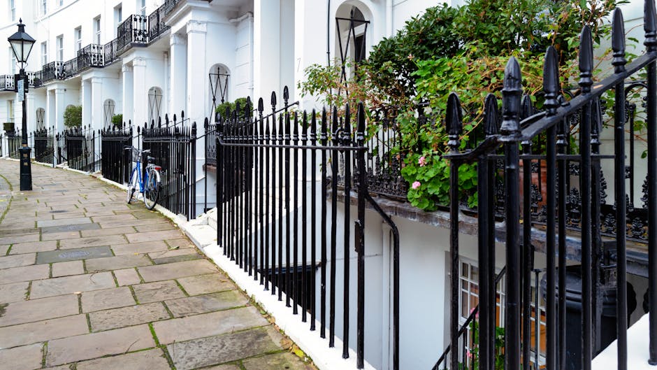 A lush, well-maintained garden in front of a stately white building with classical architectural details, including large windows and a decorative balustrade. The garden features a variety of plants,